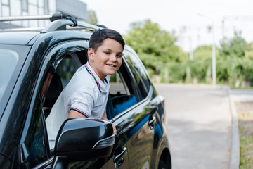 cheerful boy smiling and looking at camera from car window