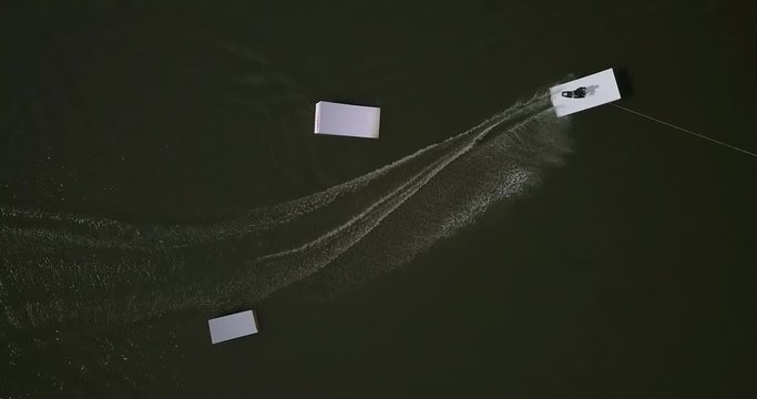 Aerial shot of a cableway in a lake with a wakeboarder making turns and tricks. Sportsman grinding and rotating on a funbox. Girl wakeboarding in wake park. Sport time summer concept.