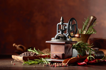 Vintage pepper mill with kitchen utensils, spices and rosemary on a old wooden table.