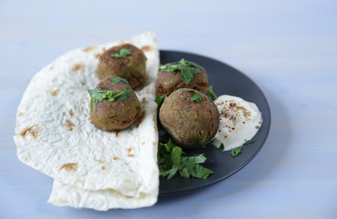 falafel with tortilla, fresh parsley and souse on the plate on a light color wooden table. Vegan tacos. Vegetarian healthy food. The concept of healthy eating. With copy space for text.