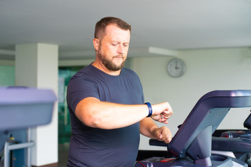 full male runs on a treadmill in the gym and looks at the smart watch. concept of weight loss and...