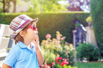 Portrait of funny curious little boy in hat and sunglasses looking up thoughtfully  outdoors in garden at sunny summer day.  Summer lifestyle.