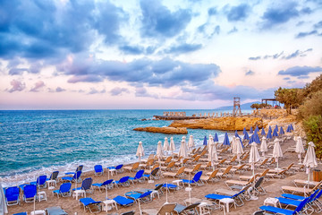 Fototapeta na wymiar Sun beds and umbrellas on an empty beach in the background of a beautiful cloudy sky in Crete Island, Greece. Concept of summer holiday, vacation and tourism.
