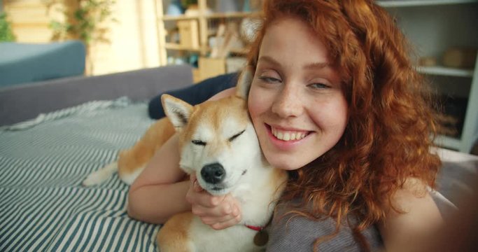 Close-up portrait of attractive young girl and pedigree dog lying on couch kissing looking at camera having fun expressing love. People and animals concept.
