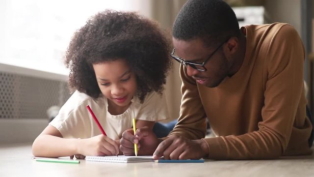 Happy african dad and cute kid girl drawing play together