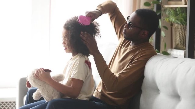 Loving black father doing brushing afro hair of kid daughter