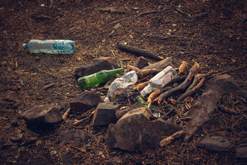 Used plastic and glass bottles surrounded by stones in the ashes after a fire. Picnic trash. Pollution of nature