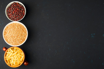 BOWL WITH RAW PASTA BUCKWHEAT BEANS ON A DARK BACKGROUND. THE CONCEPT OF HEALTHY EATING.