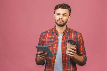 Portrait of confident young handsome man in casual with cup of coffee working on digital tablet isolated on pink background in studio.