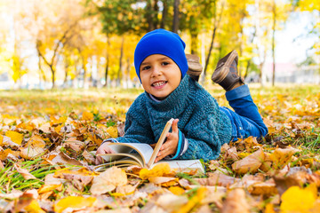 boy lying on his stomach reading a book in the fall in the Park