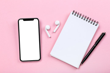 Smartphone with earphones and notepad on pink background