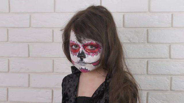 A child with a painted face for Halloween. Sad little girl with skeleton make-up shows no gesture. Child abuse.