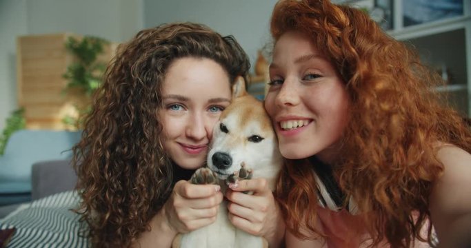 Close-up portrait of beautiful girls sisters and shiba inu dog taking selfie at home lying on bed looking at camera holding device. People and animals concept.