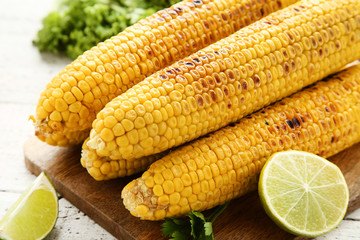 Grilled corn with lime pieces on wooden table