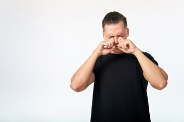 Young man suffering from allergy and scratching his eyes. Studio shot on white background. Copy space.