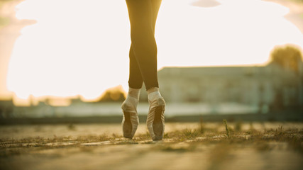 Graceful legs of young woman ballerina standing on the roof on her tiptoes - sunset