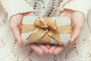 Hand hold the gift box. Present wrapped in craft paper and satin ribbon. Small parcel in a girls hands. Christmas time.
