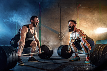 Two muscular bearded tattoed athletes training, lifting heavy weight bar in smoke at gym. Scream. Working hard. Exercise for the muscles of the back