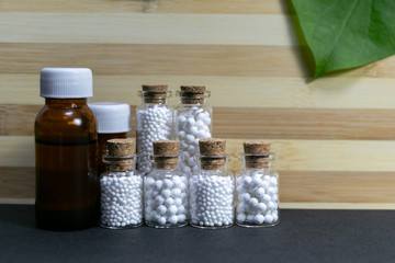 Bottles of homeopathic medicines in a row with green leaf on dark surface and wood background