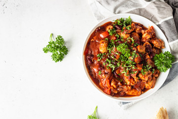 Meat stew with red beans, bell pepper and onion in tomato sauce in a white plate over light grey slate or stone background.  - obrazy, fototapety, plakaty