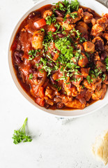 Meat stew with red beans, bell pepper and onion in tomato sauce in a white plate over light grey slate or stone background. 