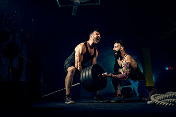 Fototapeta na wymiar Two muscular bearded tattoed athletes training, one lift heavy weight bar when other is motivating. Scream. Working hard. Exercise for the muscles of the back