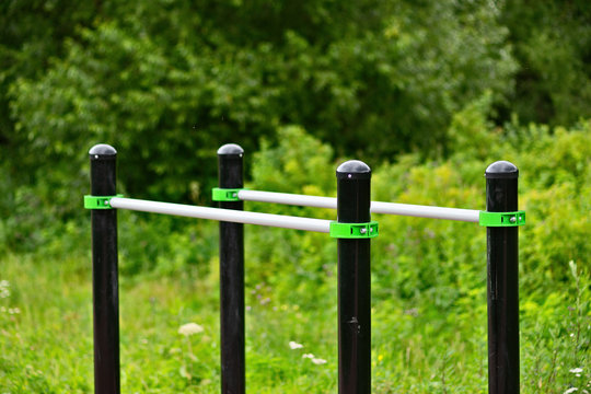 Stationary parallel horizontal bars for outdoor workout exercises. Green grass and shrubs of a public park around. Sunny summer day