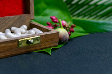 Fototapeta premium Herbal medicine capsules in wooden old box with flower bud, wild fruit and green leaf on dark background