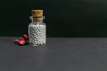 Homeopathic medicine bottle of pills with flower buds on dark background. Natural medicine concept