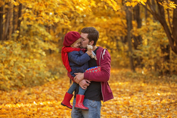 Fototapeta premium Father hugs and kisses his daughter in autumn day. The girl is holding a teddy bear.