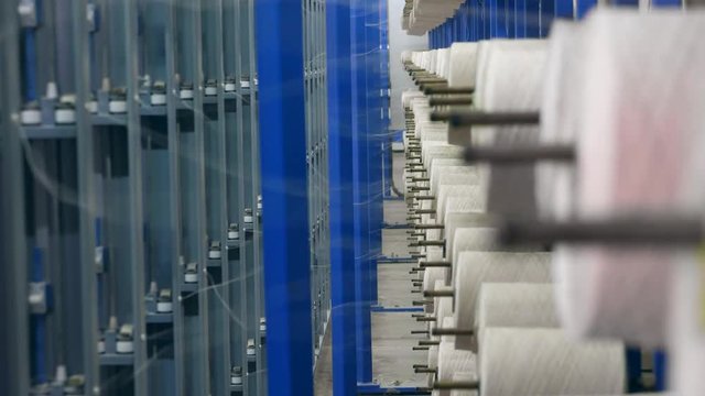 Threads on the reels are unwinding to make fabric. Textile factory equipment.