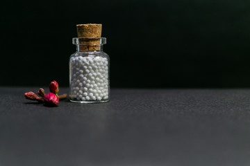 Natural Homeopathy - Vintage homeopathy medicine bottle of pills with pink flower buds on dark background