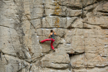 A young woman with a rope engaged in the sports of rock climbing on the rock.