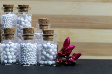 Natural Homeopathy Concept  - Vintage homeopathic medicine bottles of pills with pink flower bud on wood and dark background