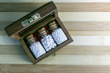 Top view image of old wooden box with homeopathic globules in glass bottles on wood background - Alternate medicine concept