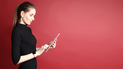 Portrait of a beautiful smiling caucasian woman working on tablet isolated on a red background