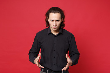 Fototapeta premium Shocked upset stylish young curly long haired man in black shirt posing isolated on red wall background studio portrait. People sincere emotions lifestyle concept. Mock up copy space. Looking camera.