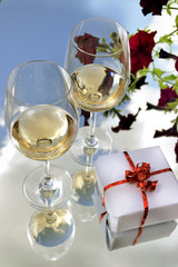 The photo shows glasses of white wine, a gift, and flowers.