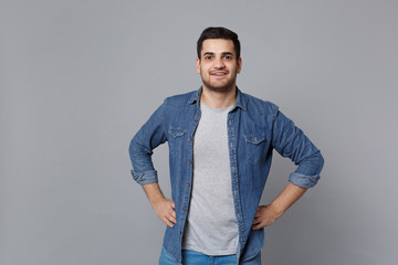 Handsome stylish unshaven young man in denim jeans shirt posing isolated on grey wall background...