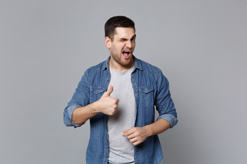 Handsome stylish unshaven young man in denim jeans shirt posing isolated on grey wall background...