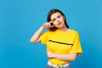 Portrait of displeased puzzled young woman in vivid casual clothes looking camera, keeping hand near face isolated on bright blue background in studio. People lifestyle concept. Mock up copy space.