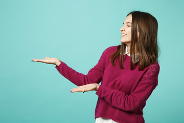 Young brunette smiling woman girl in casual clothes posing isolated on blue green wall background studio portrait. People sincere emotions lifestyle concept. Mock up pointing finger hand on copy space