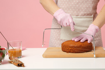 Close up cropped hands of chef cook confectioner or baker in apron white t-shirt cooking, cutting cake with tool at table isolated on pink pastel background in studio. Mock up copy space food concept.