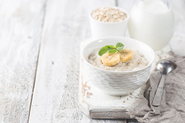 Bowl of oatmeal porridge with banana on white wooden rustic table, healthy breakfast, diet food.