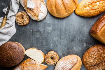 Assortment of fresh baked bread and buns on black background, top view