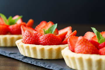 Tartlets with custard, strawberries and mint served on a slate plate