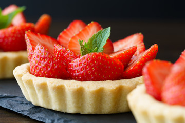 Tartlets with custard, strawberries and mint served on a slate plate