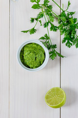 Guacamole from avocado, lime, cilantro and garlic  in white bowl on wooden table. Flat lay, closeup.