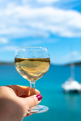 hand with glass of white wine served outside on balcony with sea view