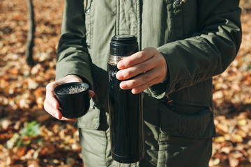 Person with a thermos in his hands in the autumn forest. The man is going to drink goyang drink - tea or coffee to keep warm.